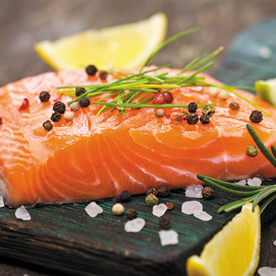 Raw salmon fillet garnished with lemon slices, fresh herbs, and colorful peppercorns on a rustic wooden board.