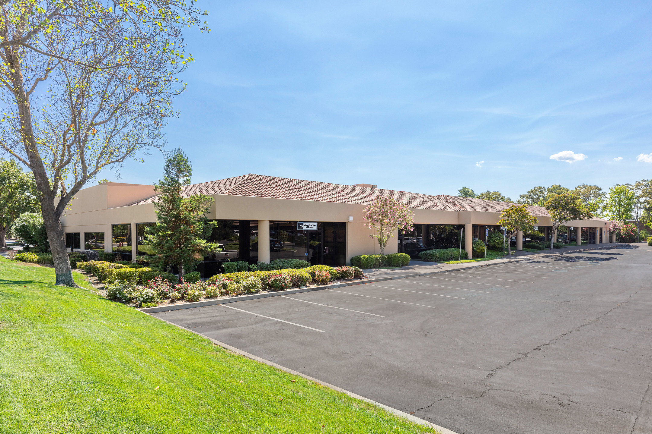 New Nexus Office - Single-story office building with large windows, surrounded by landscaping and trees, next to an empty parking lot under a clear blue sky.